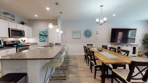 A modern kitchen with granite countertops, stainless steel appliances, and a dining area with a wooden table and chairs. - Shared Heated Pool with Water Slide, Golf Cart Access (Port Aransas)