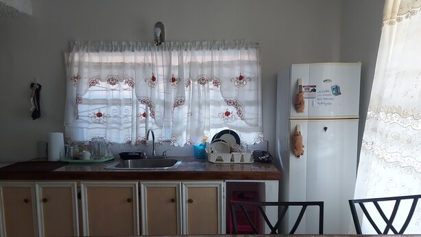A kitchen with a sink, cabinets, a refrigerator, and a window with a floral curtain.