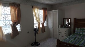 A bedroom with a bed, a dresser, a fan, and a window with curtains.