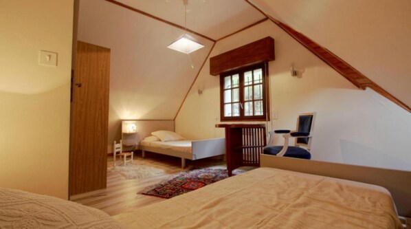 A bedroom with a sloped ceiling, a bed, a desk, a chair, and a window.