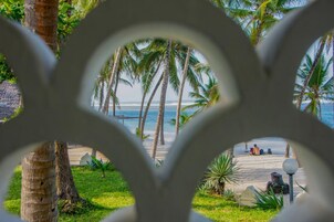 A beach view through a decorative archway, featuring palm trees and a sandy path leading to the ocean.