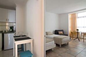 A compact hotel room with a kitchenette, a bed with a bedside table, and a small dining area. - Hotel Idafe (Las Palmas de Gran Canaria)