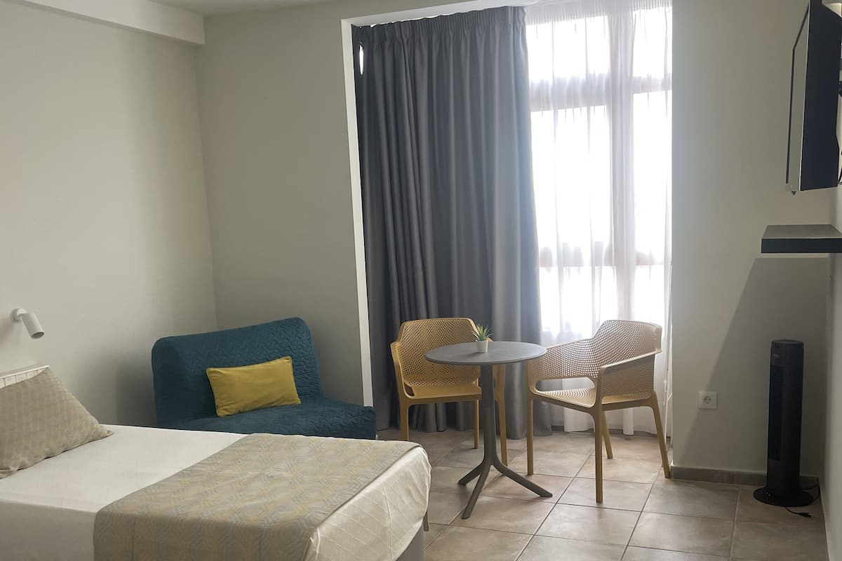 A hotel room with a bed, a sofa, a small table with chairs, and a TV mounted on the wall.