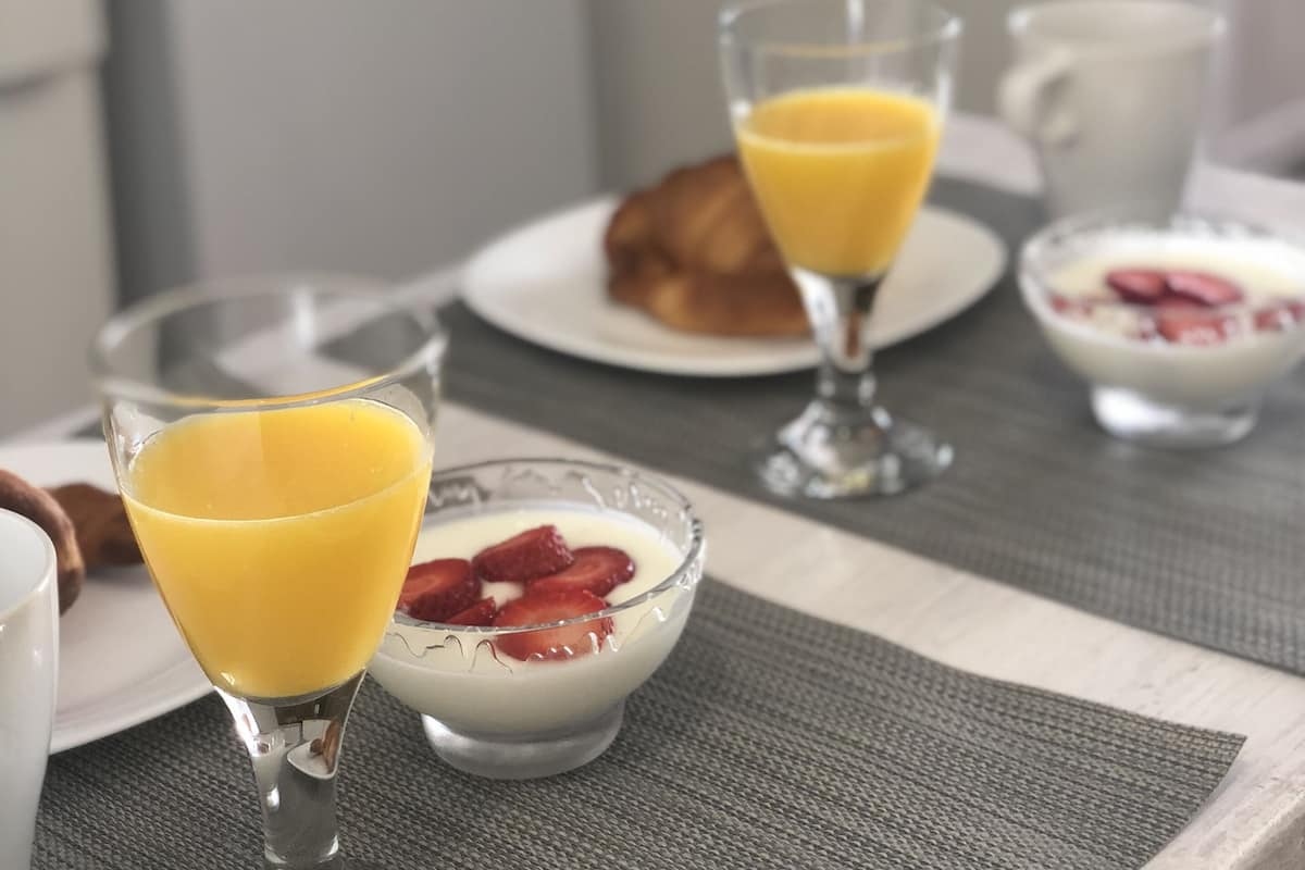 A breakfast setting with a glass of orange juice, a bowl of yogurt with strawberries, and a croissant on a table.