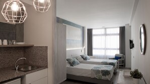 A modern hotel room with a kitchen area, two beds with matching decor, a seating area, and a large window with curtains. - Hotel Idafe (Las Palmas de Gran Canaria)