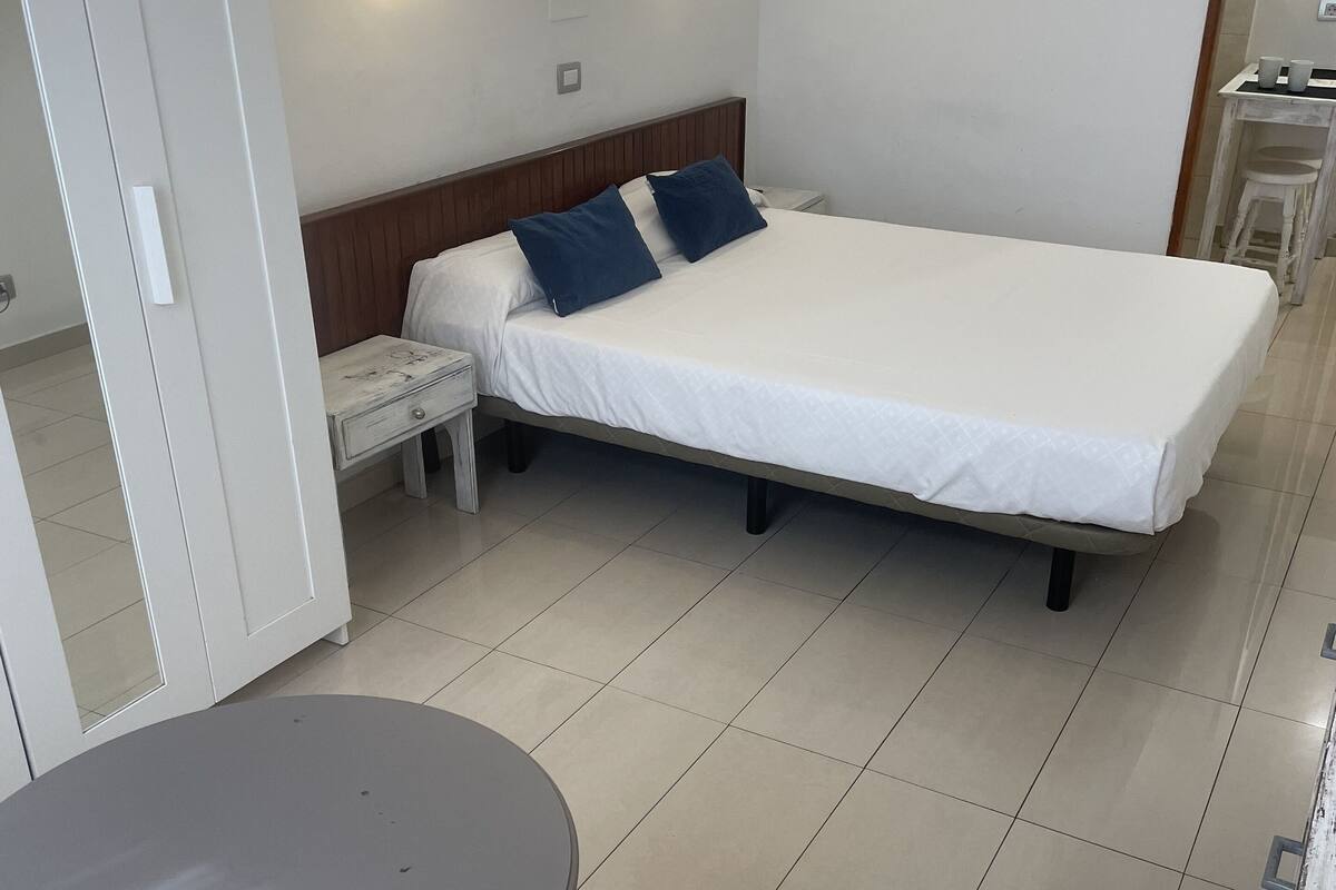 A hotel room with a bed, bedside tables, a small table, and a chair.