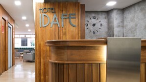 A hotel reception desk with a wooden finish, a clock on the wall, and a sign that reads "HOTEL IDAFE". - Hotel Idafe (Las Palmas de Gran Canaria)