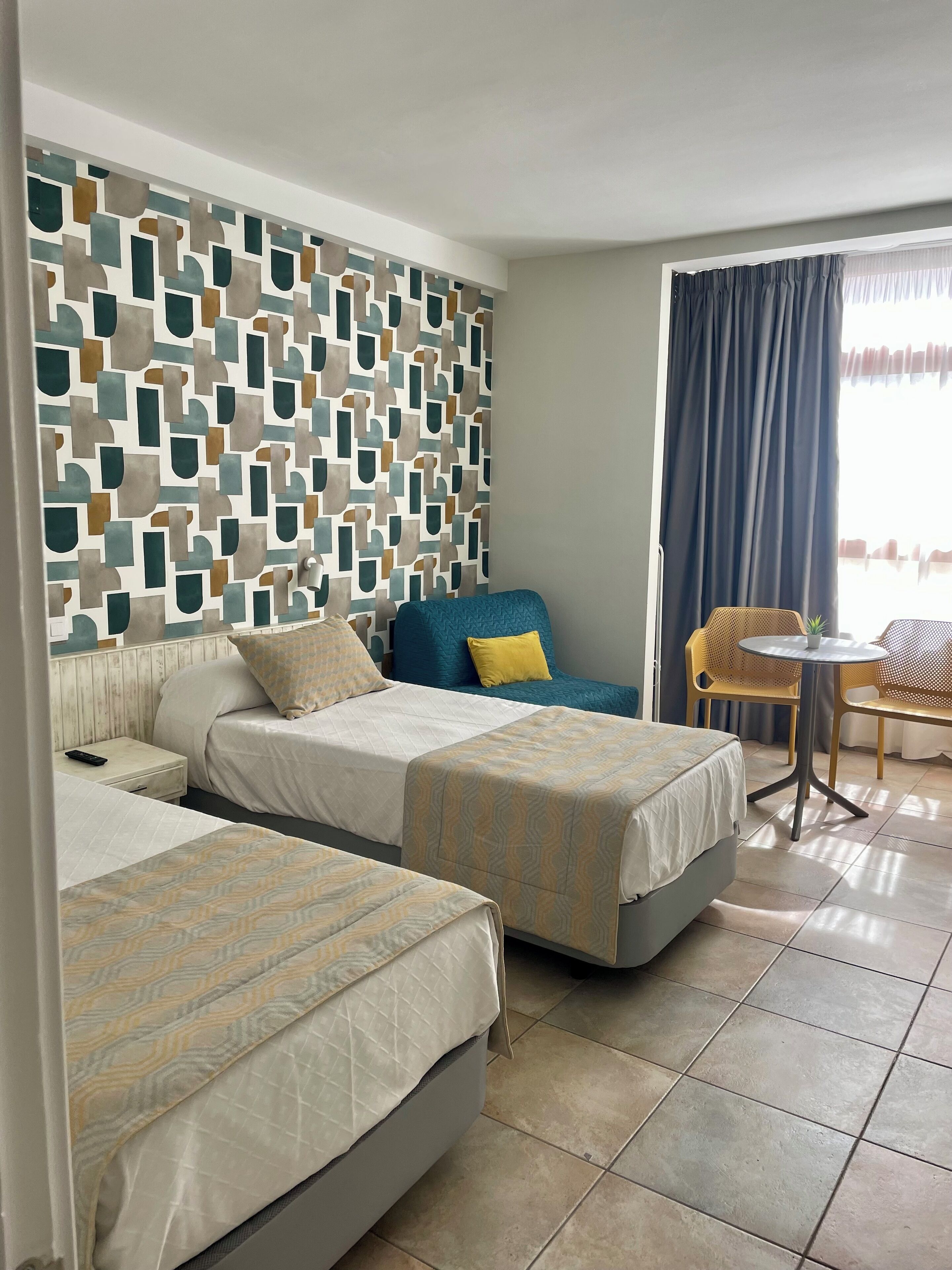 Een hotelkamer met twee bedden, een klein tafeltje, een stoel en een behangen muur.