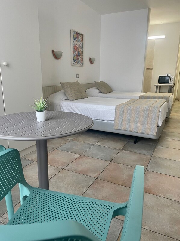Una habitación pequeña y limpia con una cama, una mesa con una planta en maceta y un microondas.