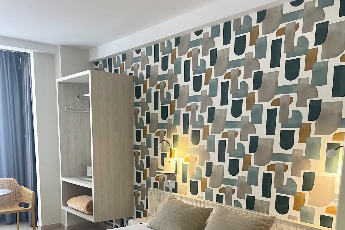 A modern hotel room with a large bed, a wardrobe, a bedside table, and a wall with a geometric pattern.