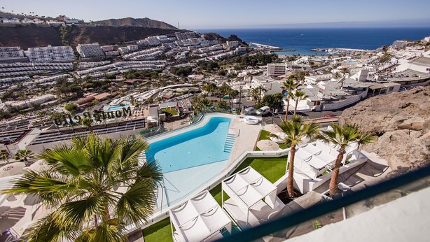 A resort with a large swimming pool, palm trees, and a view of the ocean. - Servatur Hartaguna - Adults Only (Mogan)