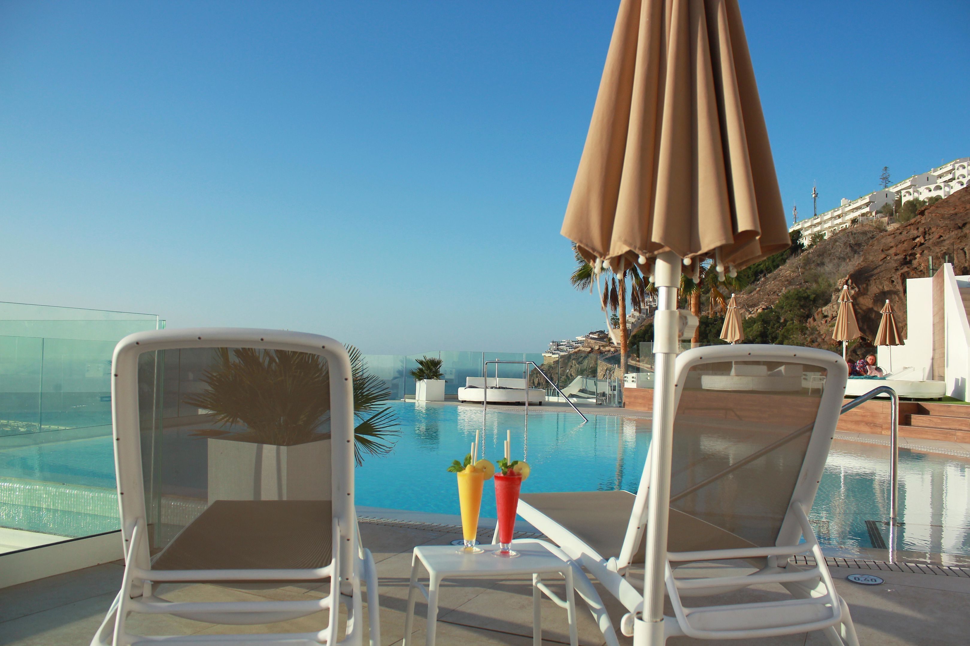 A poolside area with two lounge chairs, a table with drinks, and a large umbrella.