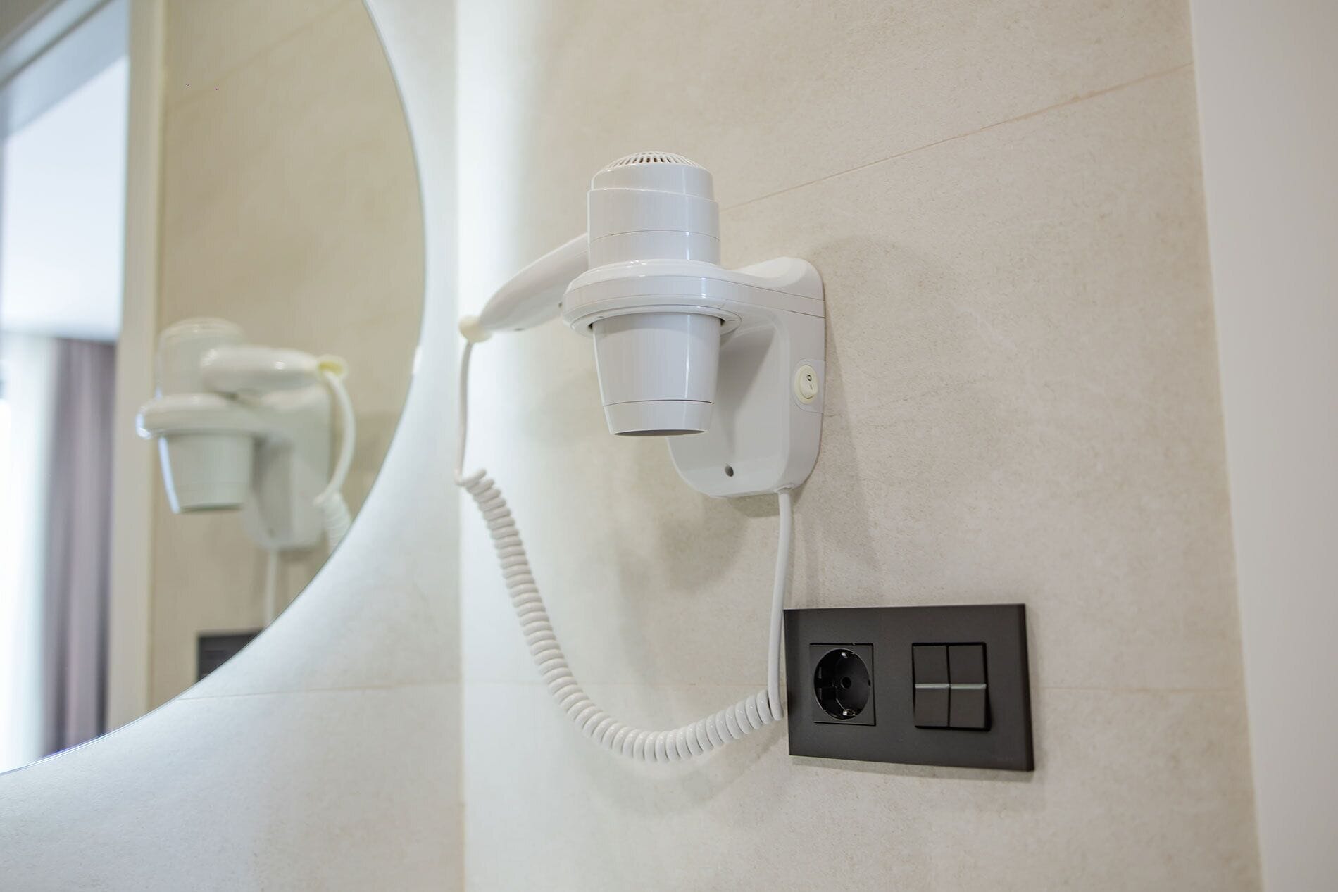 A hair dryer mounted on a wall with a power outlet below it.