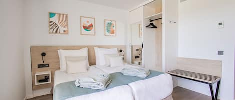 A modern bedroom with a wooden headboard, a bed with white linens, a bedside table with a lamp, and a walk-in closet.