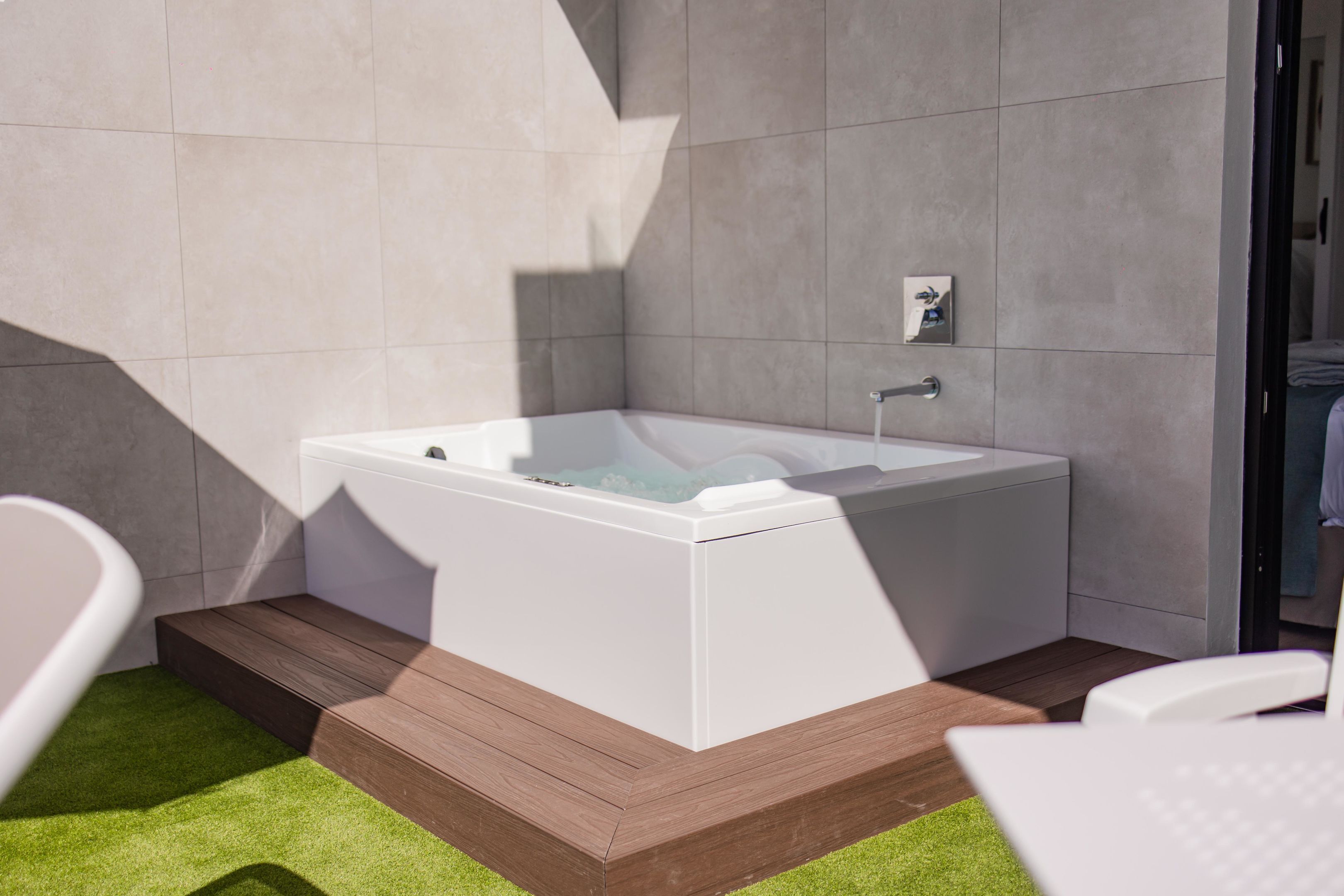 Een moderne badkamer met een vrijstaand bad, houten trapjes en een vloer van kunstgras in het groen.
