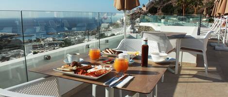 A balcony with a table set for breakfast, overlooking a coastal cityscape.