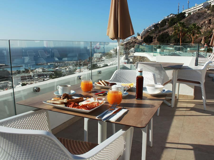 A balcony with a table set for breakfast, overlooking a coastal cityscape.