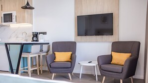 A modern living area with a sofa and armchairs, a small round table, a TV mounted on the wall, and a kitchen area with a microwave and coffee maker. - Servatur Hartaguna - Adults Only (Mogan)