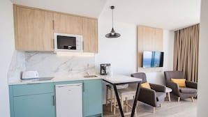 A modern kitchen with a built-in microwave, a coffee maker, and a dishwasher. There is a dining area with a table and chairs, and a TV mounted on the wall. - Servatur Hartaguna - Adults Only (Mogan)
