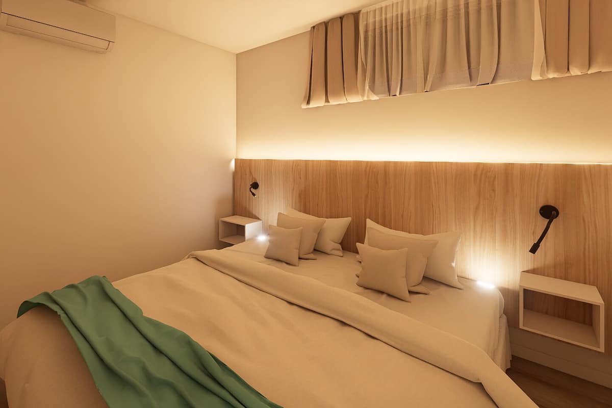 A modern bedroom with a wooden headboard, a bed with multiple pillows, bedside tables, and a wall-mounted light fixture.