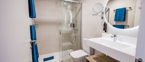 Une salle de bain moderne avec une douche à parois de verre, un lavabo blanc et un miroir doté d’un cadre rond.