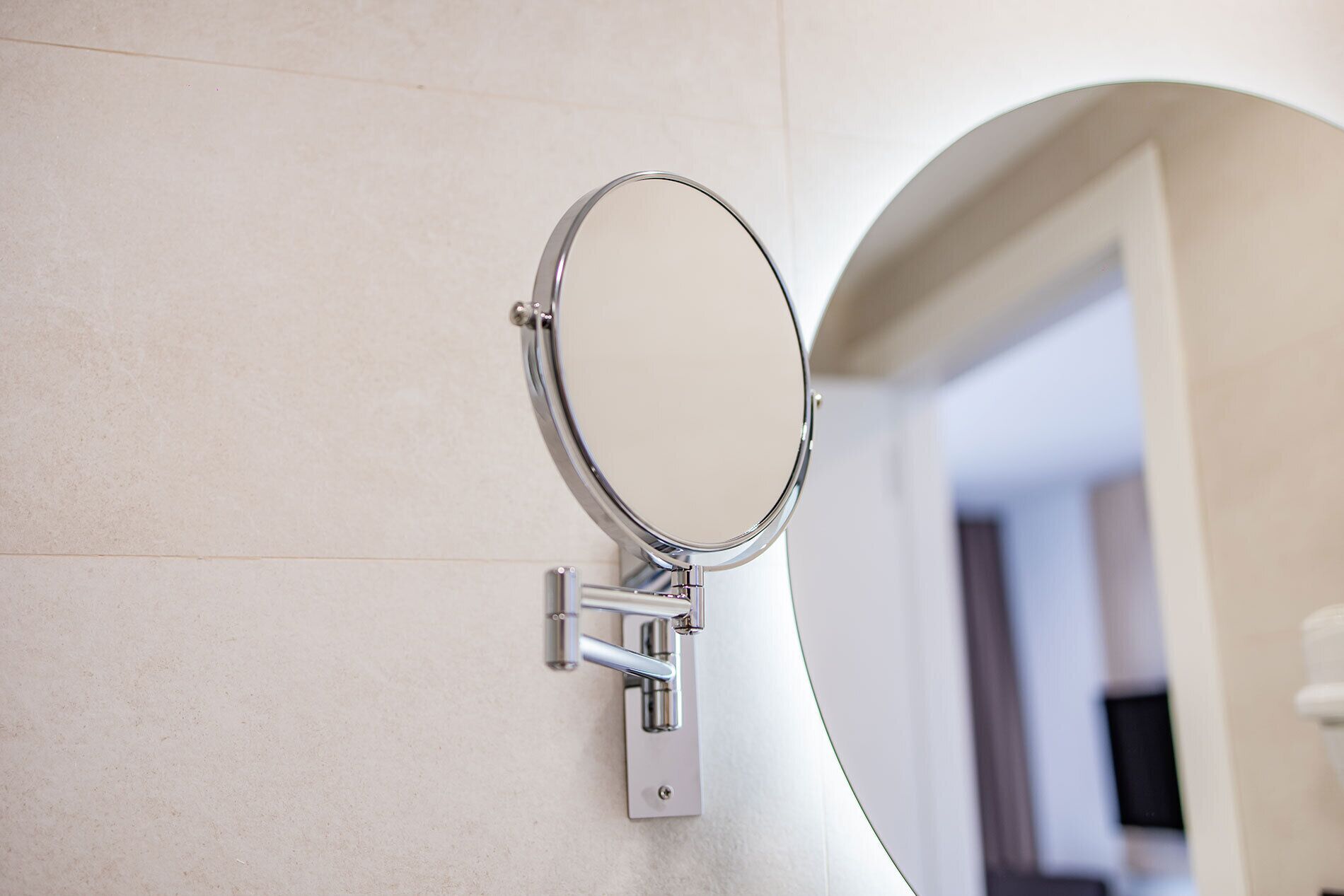 Espejo montado en la pared de un baño, con pared de azulejos y una puerta que da a otra habitación.