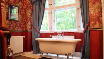 Un baño con una bañera independiente, una ventana con cortinas y un radiador.