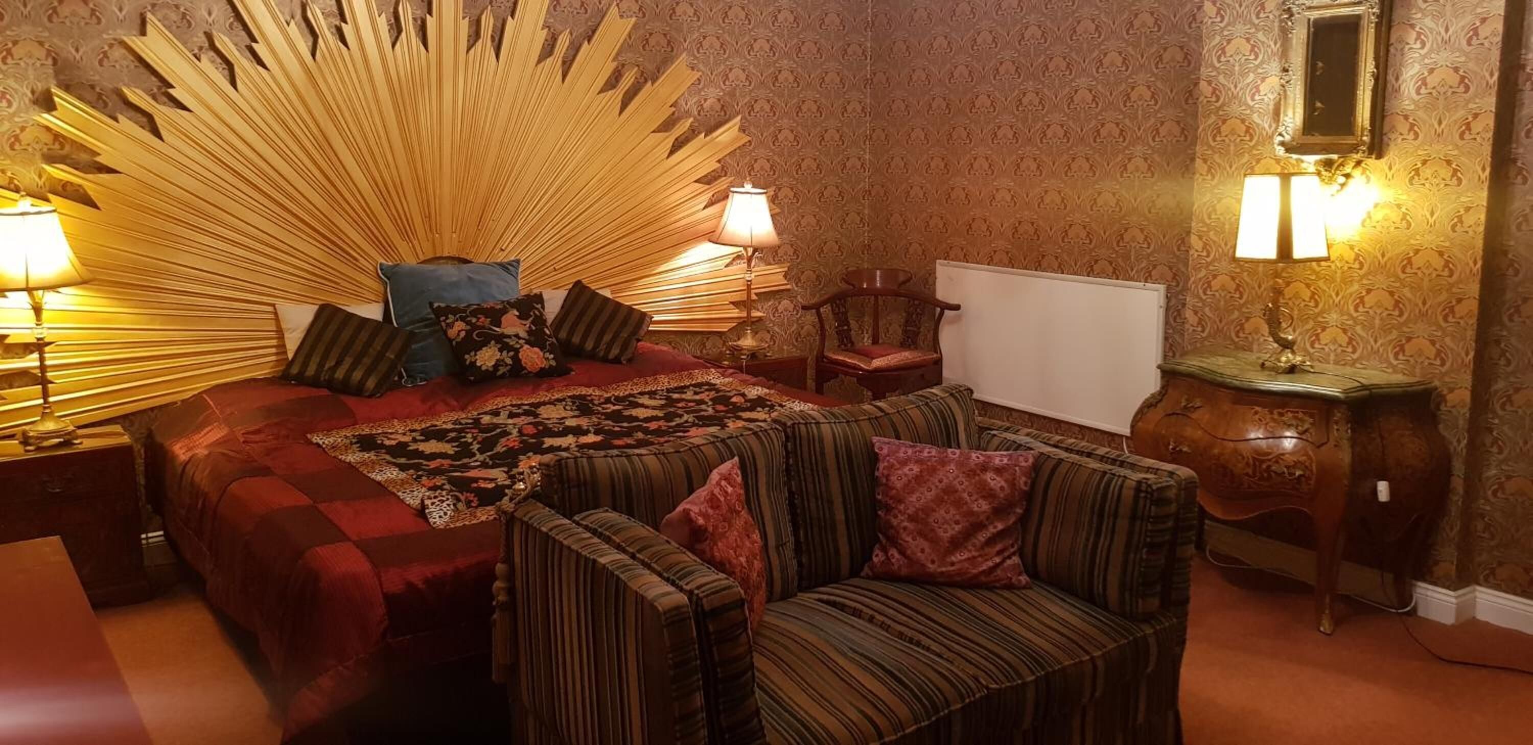 A bedroom with a large bed, two bedside tables with lamps, a chair, a small table, and a mirror on the wall.
