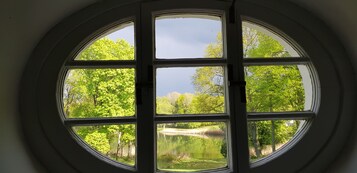 Una ventana circular de seis cristales que da a un estanque rodeado de frondosos árboles verdes.