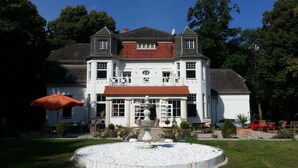 A large, two-story house with a symmetrical facade, a central entrance with a white porch, and a circular gravel garden with a fountain. - Villa am Stechlin (Stechlin)