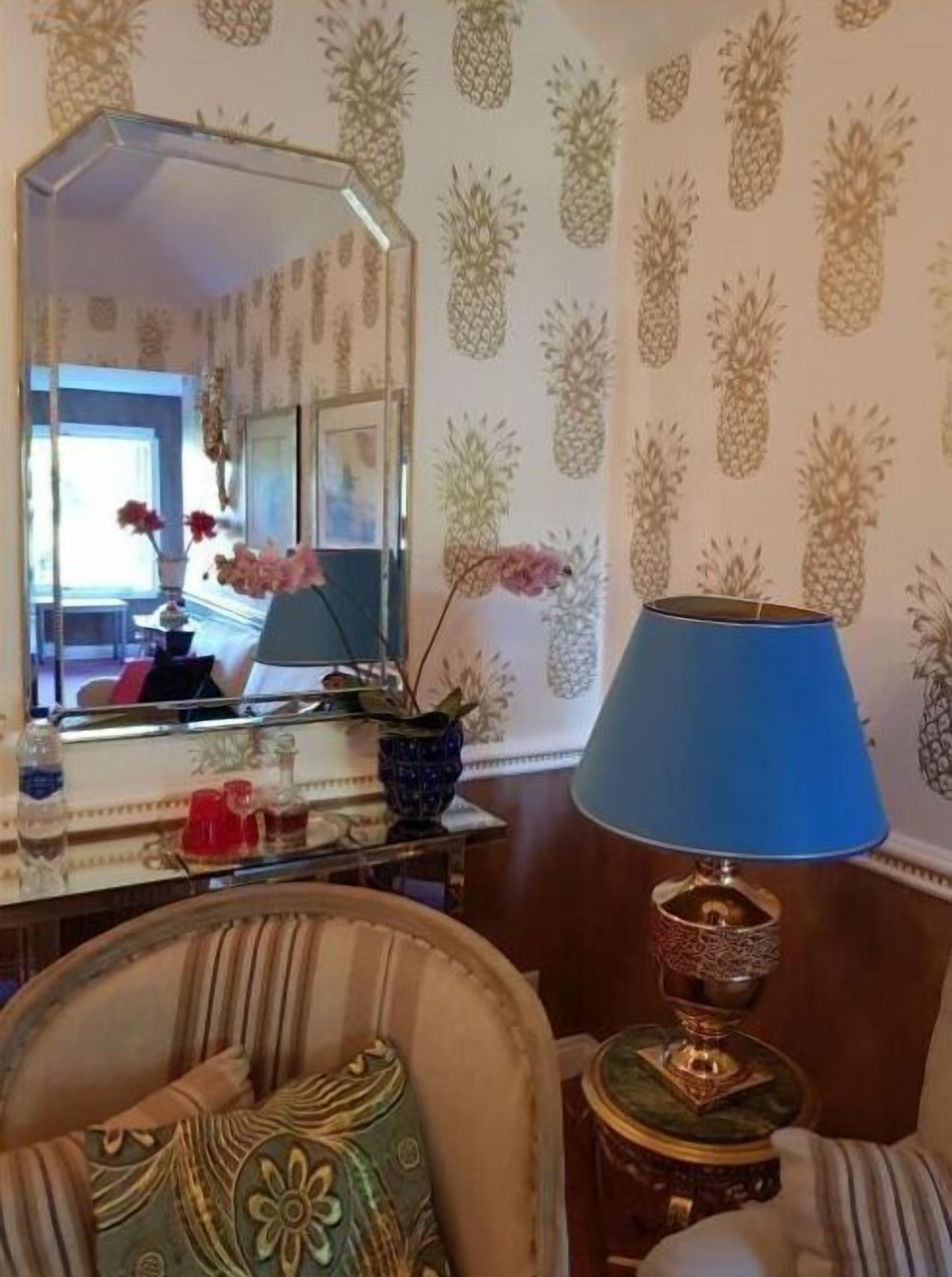Una habitación con espejo, lámpara azul, una silla decorativa y papel tapiz estampado.