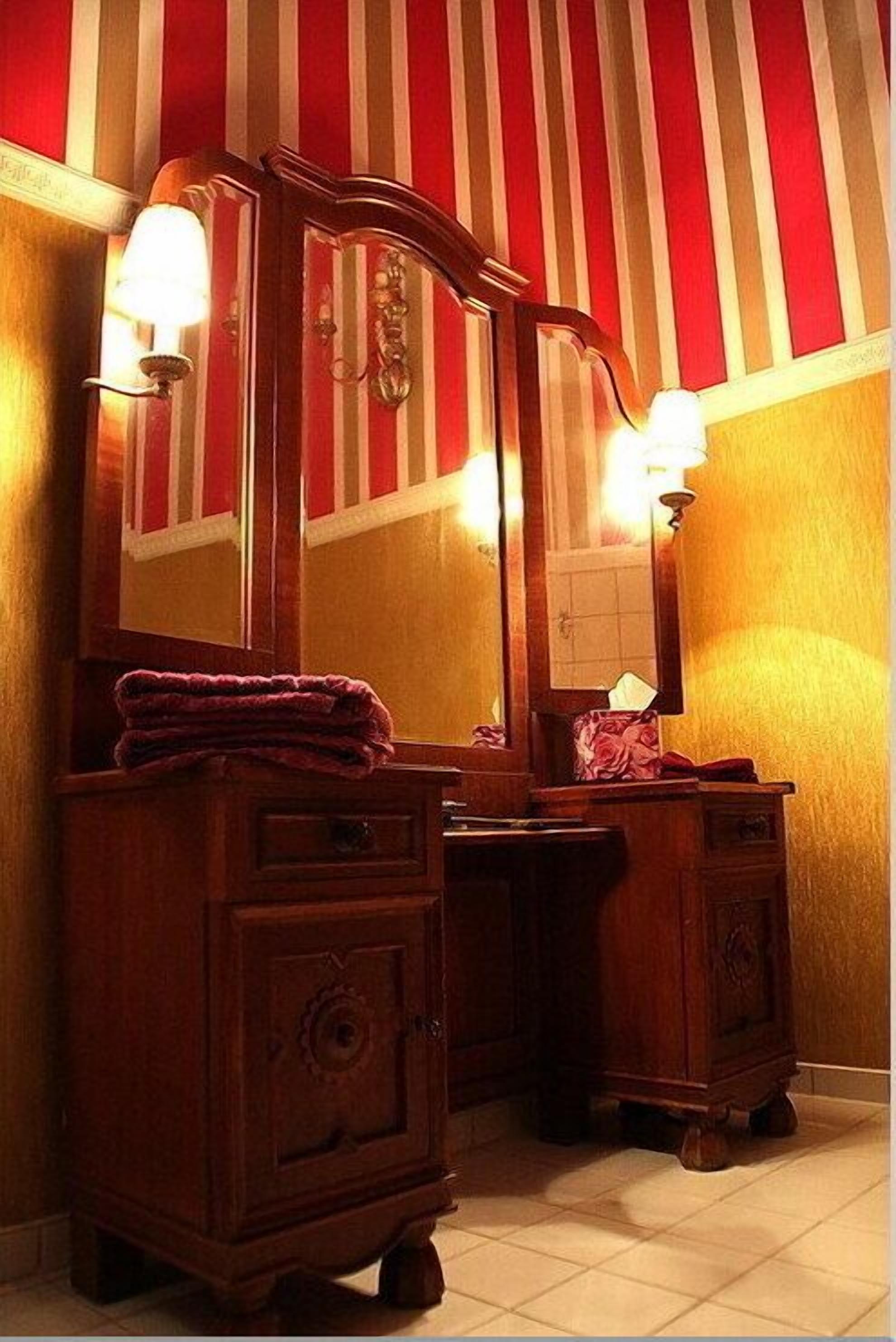 Un baño con tocador de madera, un espejo grande y papel tapiz a rayas.