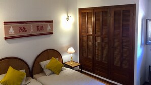 Une chambre avec deux lits, des têtes de lit en bois, une table de chevet avec une lampe, une armoire en bois et un panneau décoratif mural.