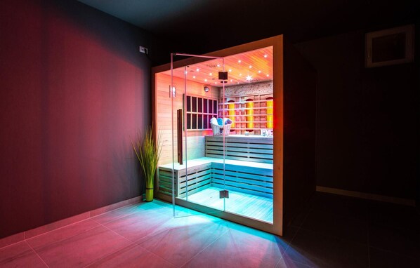 Une salle de spa moderne avec une paroi en verre, des bancs en bois et un sauna fixé au mur.