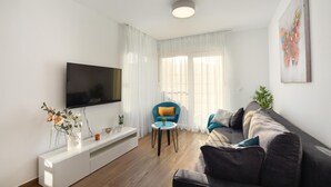Uma sala de estar moderna com uma televisão de tela plana, um sofá, uma poltrona azul e uma mesa de centro.