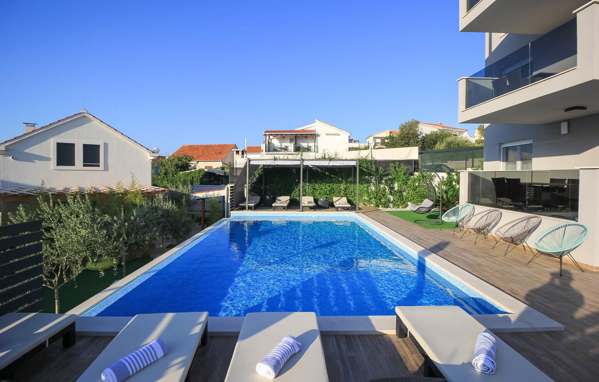 Une piscine dotée de chaises longues et d’une pergola, entourée d’immeubles d’habitation.