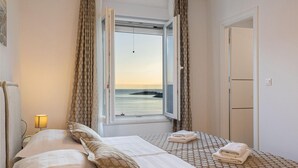 Quarto de hotel com cama, janela com cortinas e vista para o mar, e uma porta.