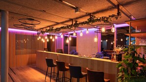 A bar area with wooden bar counter, bar stools, pendant lighting, and hanging plants. - Hotel Bergamo (Ludwigsburg)
