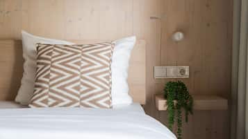 Ein Schlafzimmer mit einem hölzernen Kopfteil, einem Bett mit weißer Bettwäsche, einem gemusterten Kissen, einem Nachttisch mit Steckdose und einer hängenden Pflanze.
