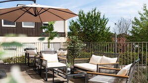 An outdoor patio with wicker furniture, a large umbrella, and a view of a building with windows. - Hotel Bergamo (Ludwigsburg)