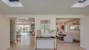A spacious living area with a central console table, a dining area with a chandelier, and a view through an open door to a patio. - Gulf Access, Heated Pool with Safety Fence -Villa Everlasting Sunshine - Roelens (Cape Coral)