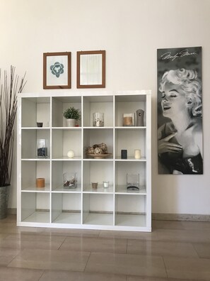 A white shelving unit with various decorative items, a framed picture, and a large poster on the wall. - Hotel Augustus Milano Marittima (Cervia)