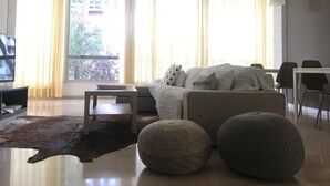 A modern living room with a sofa, ottomans, a coffee table, and a TV. - Hotel Augustus Milano Marittima (Cervia)