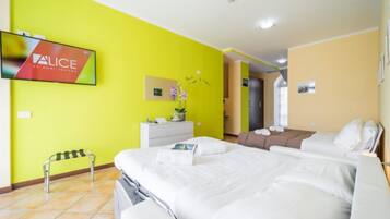 A hotel room with a bed, a TV mounted on the wall, a small table with a plant, and a bench.
