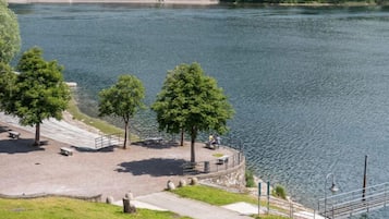Um parque à beira-rio com bancos, árvores e uma trilha para caminhada.