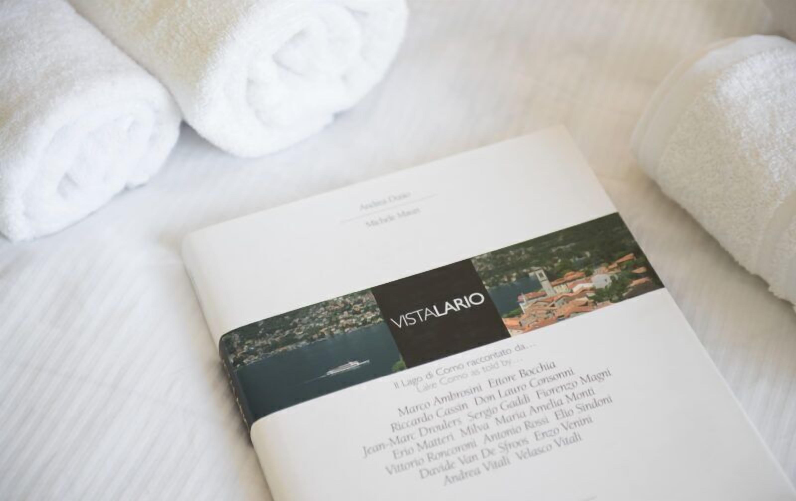 A book titled "VISTALARIO" with a list of names on its pages, placed on a white textured surface with rolled white towels.
