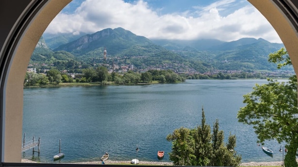 A lake with mountains in the background, a clear sky, and a few boats on the water. - Bluelake Inn - Ostello (Olginate)
