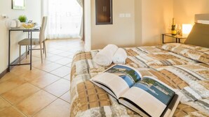 A hotel room with a bed, a desk with a chair, a small table with a bottle and glasses, and a window with curtains. - Bluelake Inn - Ostello (Olginate)
