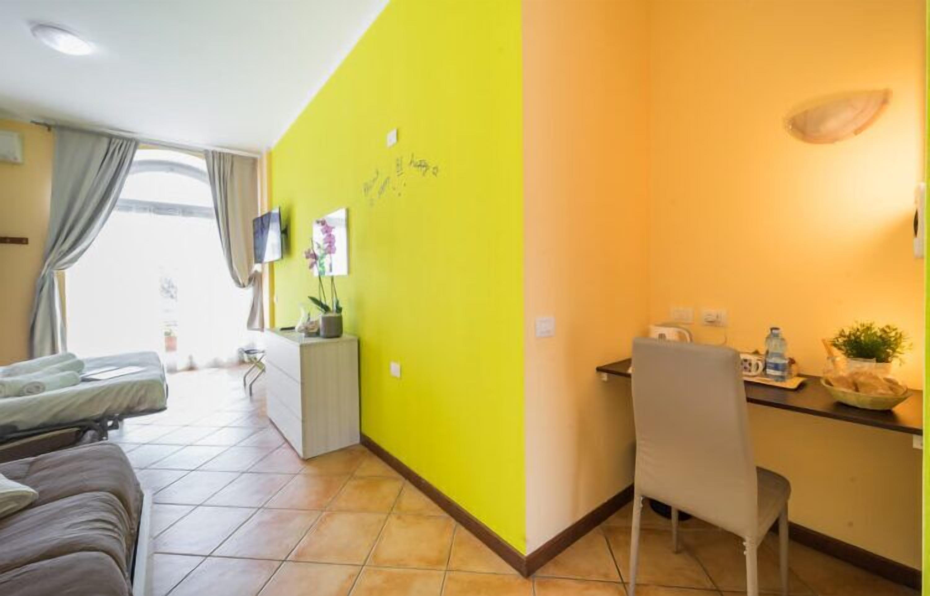 Quarto de hotel com cama, escrivaninha, cadeira, televisão e janela com cortinas.