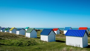 Une rangée de cabanes de plage colorées, surmontées de toits en métal, se dressant sur fond de ciel bleu azur et de mer.